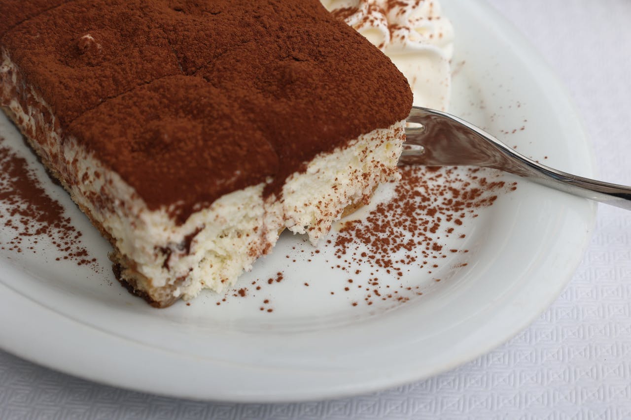 An appetizing slice of tiramisu covered in cocoa powder on a white plate.