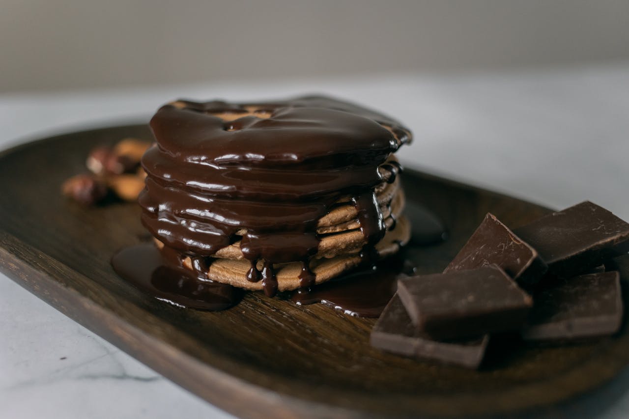 About Delicious sweet pancakes and melted chocolate on top on wooden board with bar pieces on white table